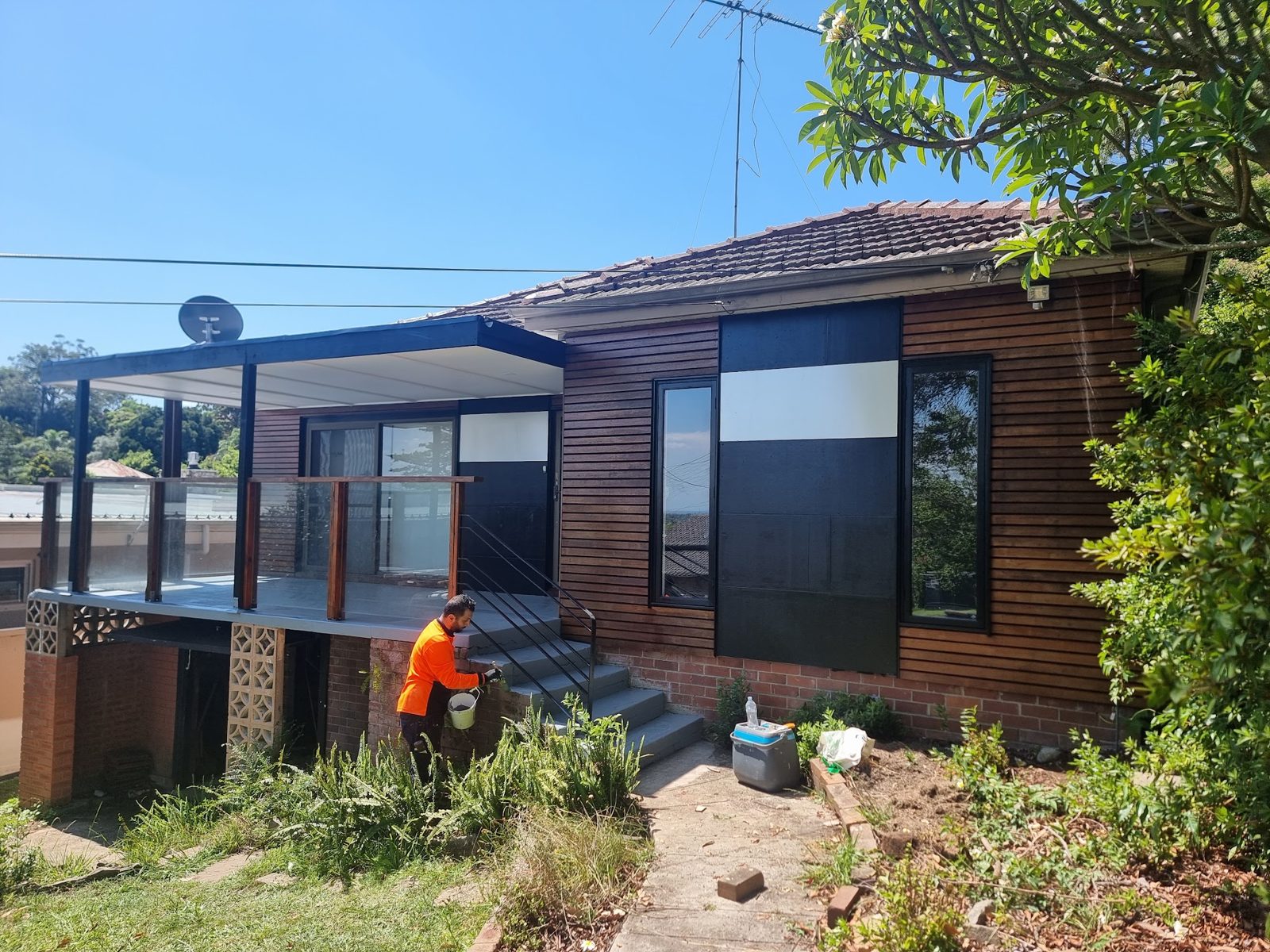 Painter in hi-vis painting the brick steps of a timber-clad house